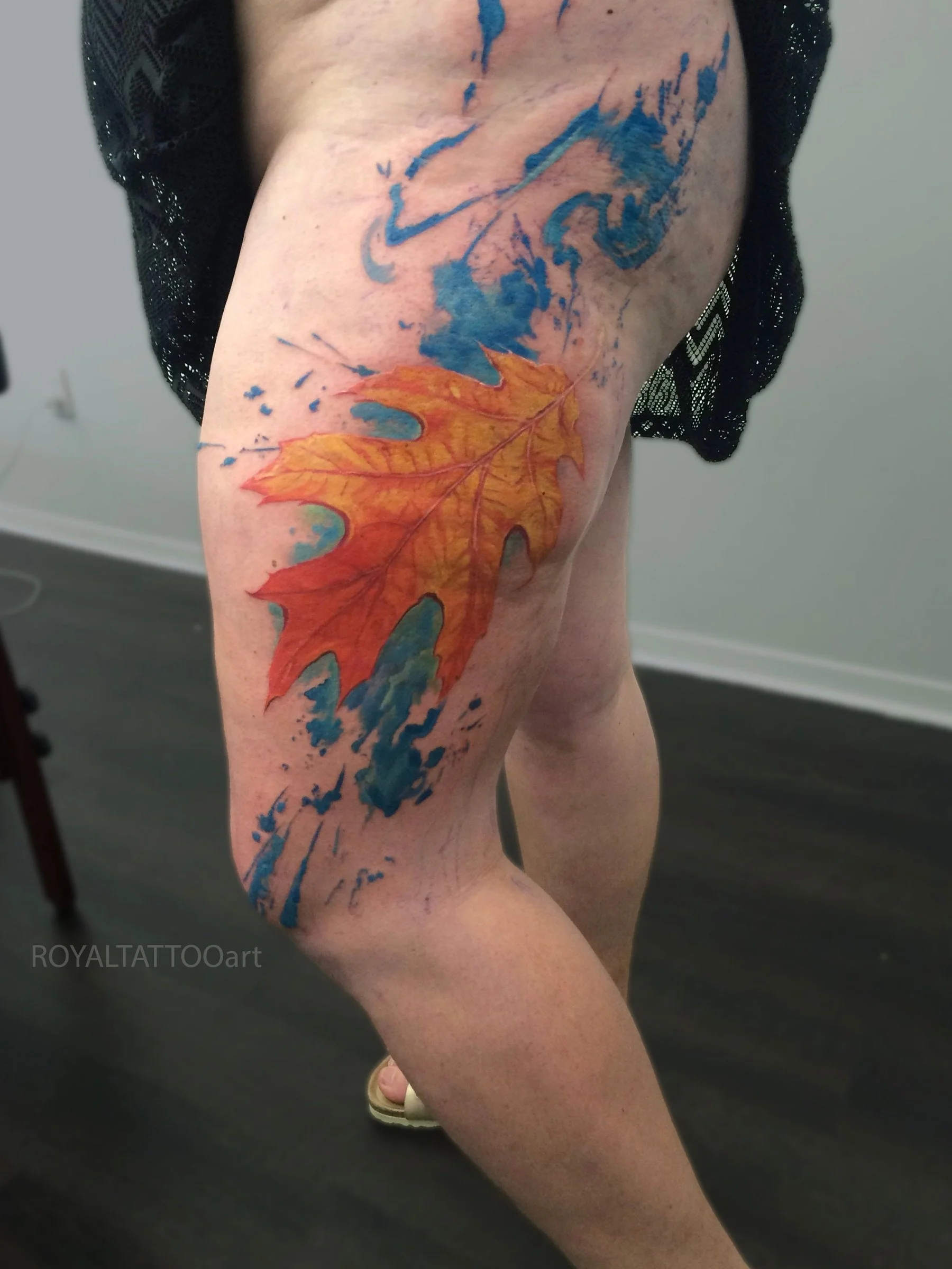 Watercolor abstract tattoo with orange and blue tones on the thigh, painterly brush strokes by Royal Jafarov at Royal Tattoo Art