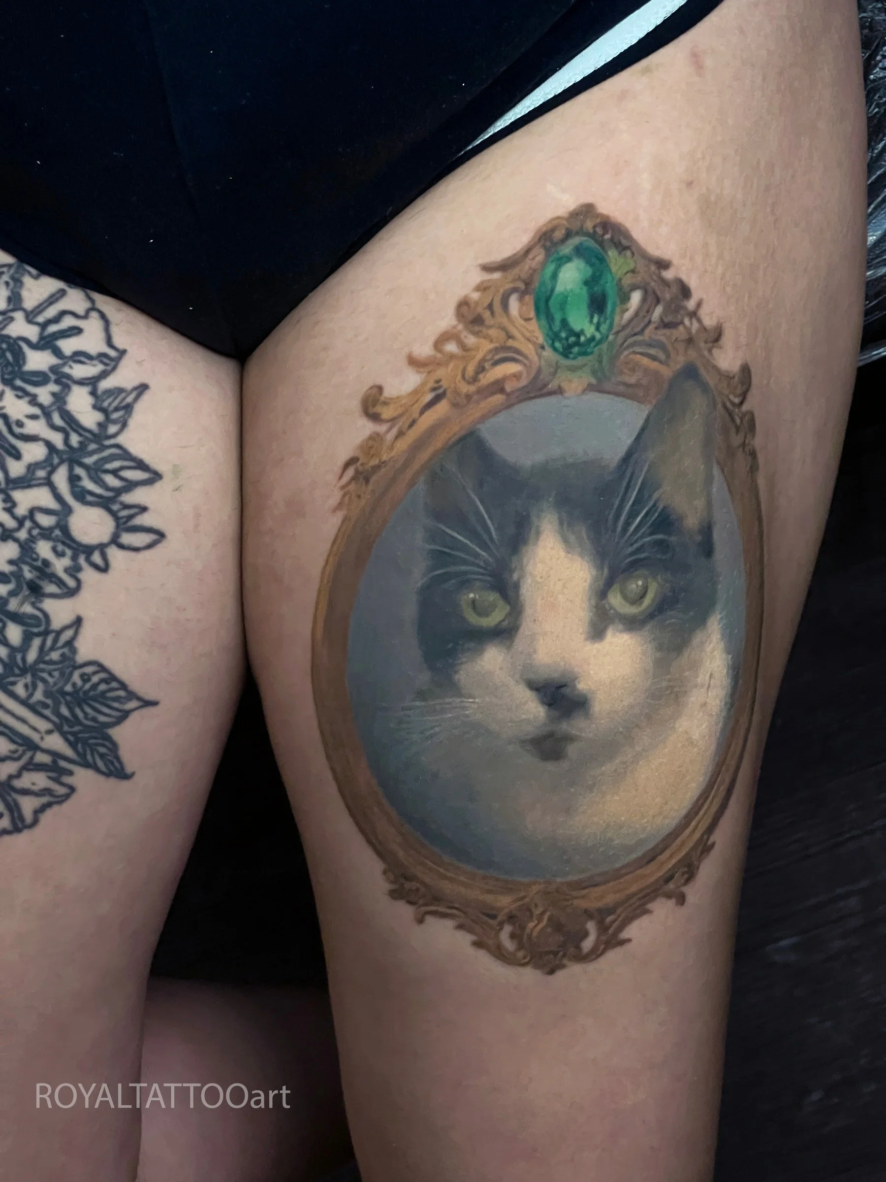 Exquisite color realism cat portrait tattoo framed in an ornate style on the thigh, tattooed in NYC. This elegant pet memorial piece from Royal Tattoo Art captures the beauty and grace of your cat with stunning photorealistic detail.