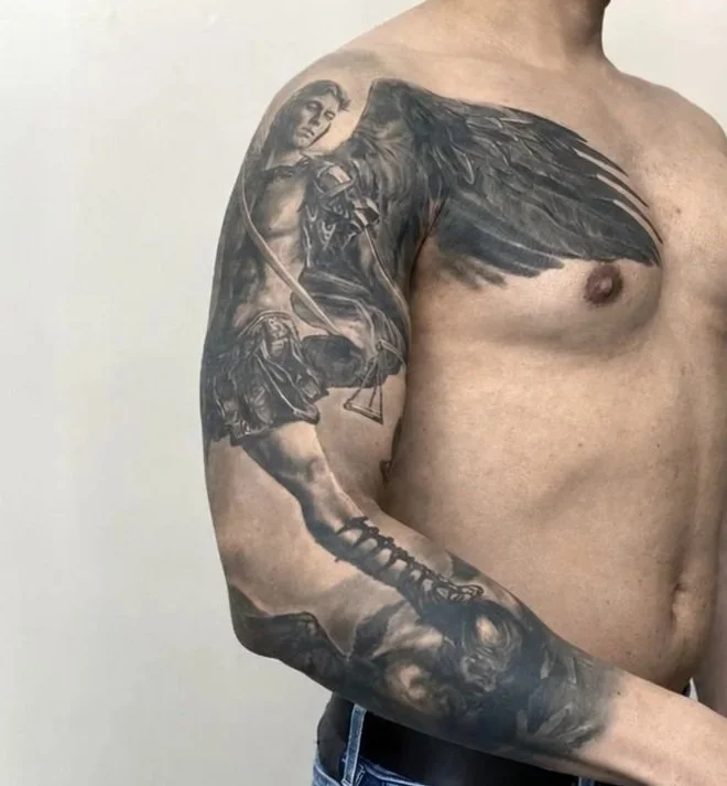 Black-and-grey realism sleeve tattoo featuring Saint Michael the Archangel with a sword and dramatic wings.
