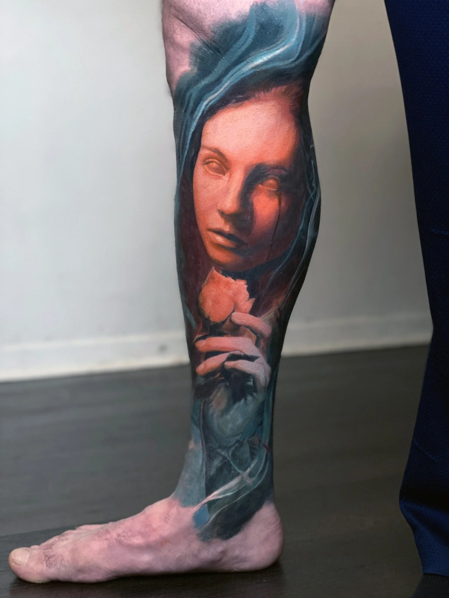 A dreamlike female face emerges from oceanic waves in this color realism leg tattoo.