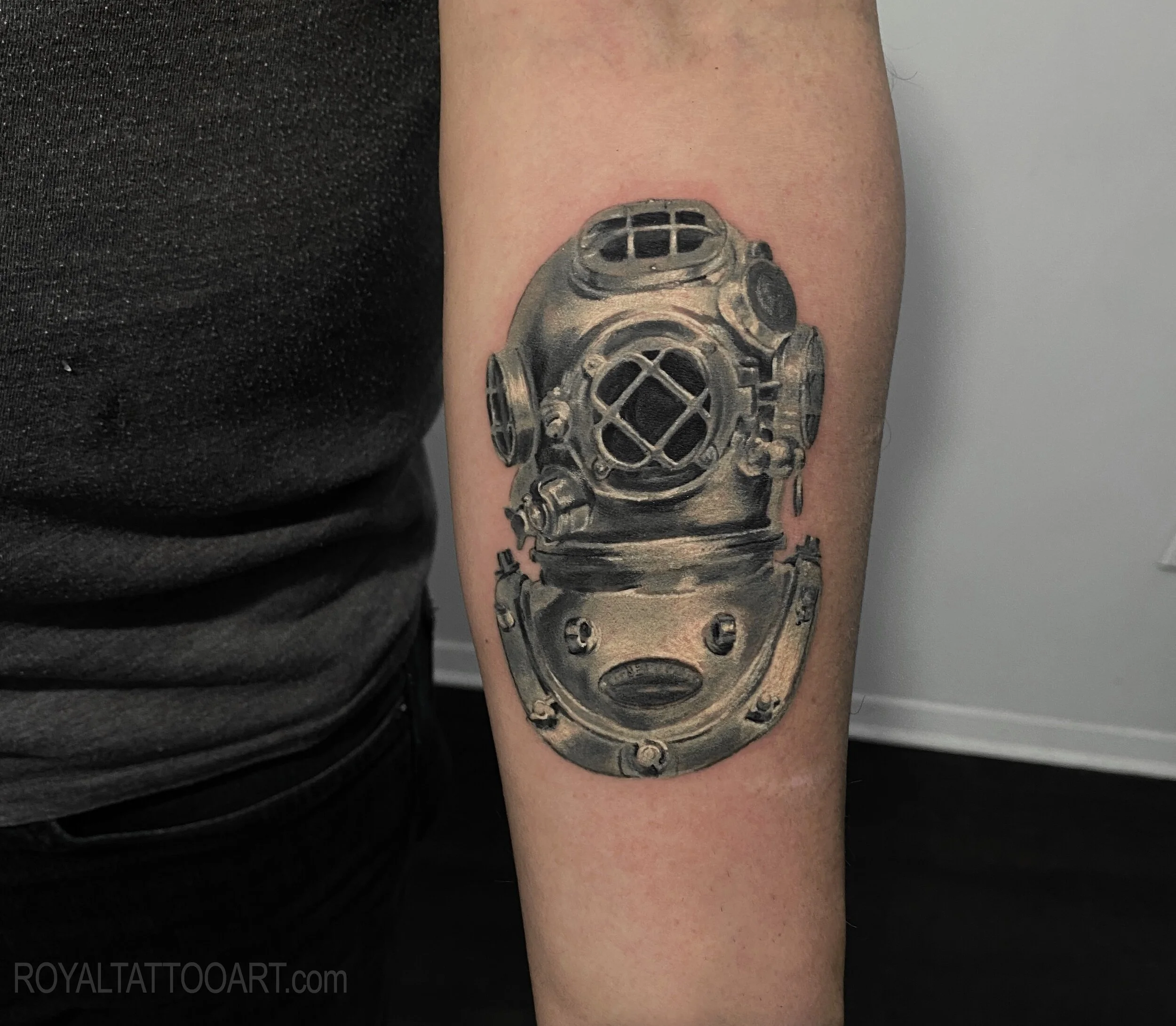 Vintage Diving Helmet Forearm Tattoo – A stunning forearm tattoo of a classic vintage deep-sea diving helmet, rendered in black and grey realism. The metalwork detail and reflective quality of the helmet are captured with incredible precision by Roya