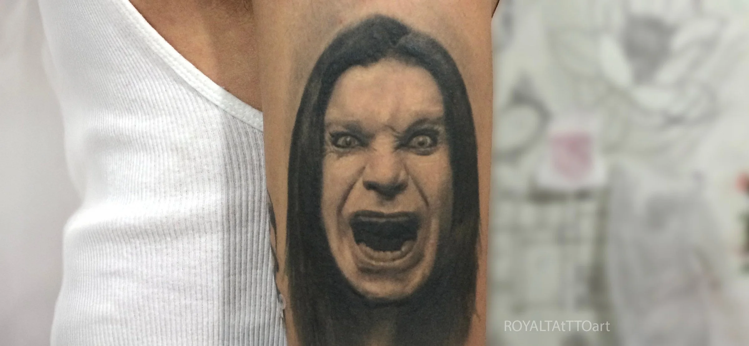 Black and grey Ozzy Osbourne portrait tattoo on the upper arm, capturing his intense expression with bold contrast and realistic detail by Royal Jafarov in NYC