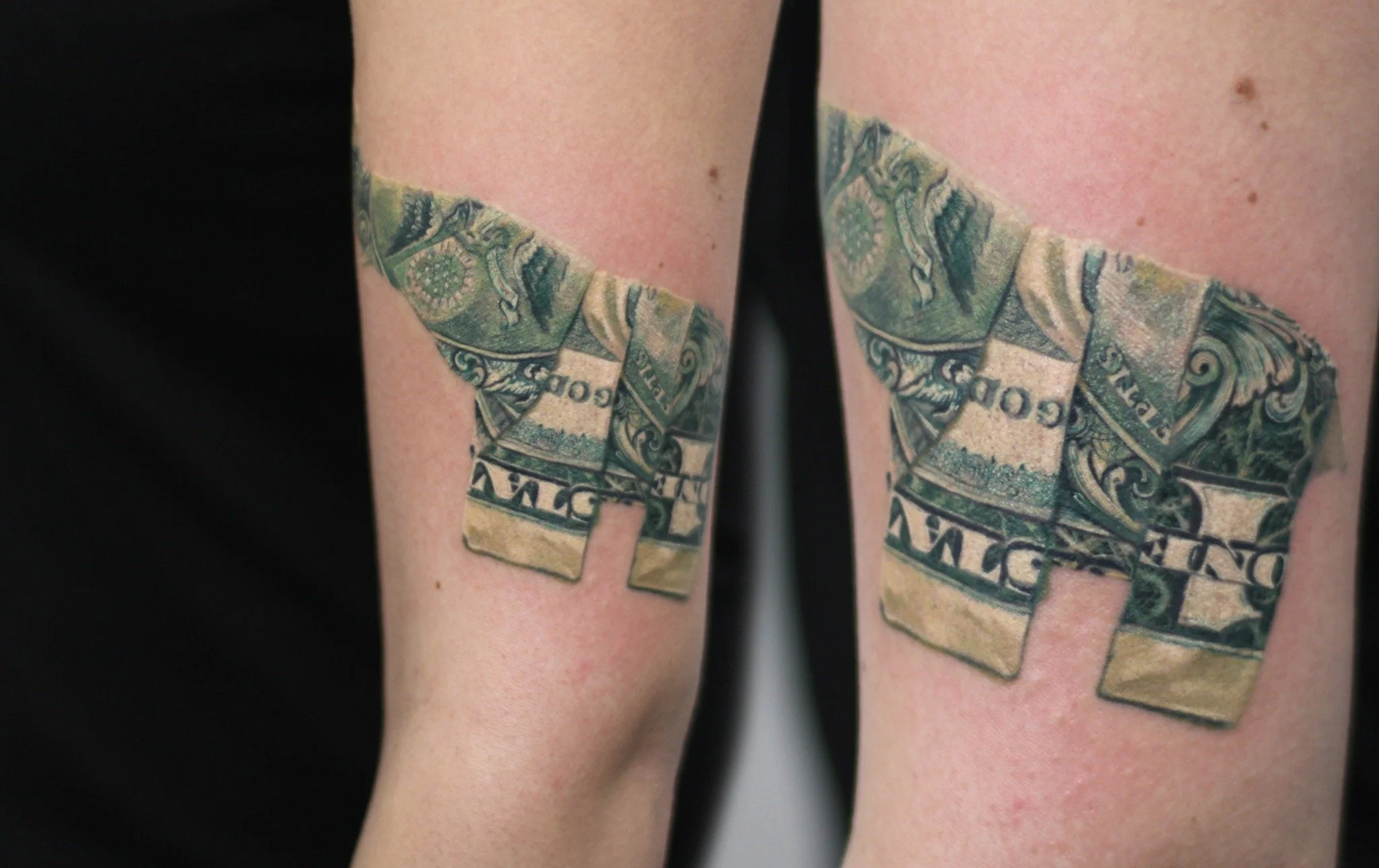 Matching elephant tattoos formed from detailed dollar-bill imagery on upper arm , combining realistic engraving textures with a creative geometric design.