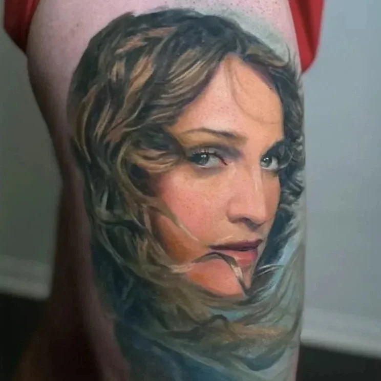 Color realism portrait tattoo of Madonna on the leg, rendered with soft painterly shading.