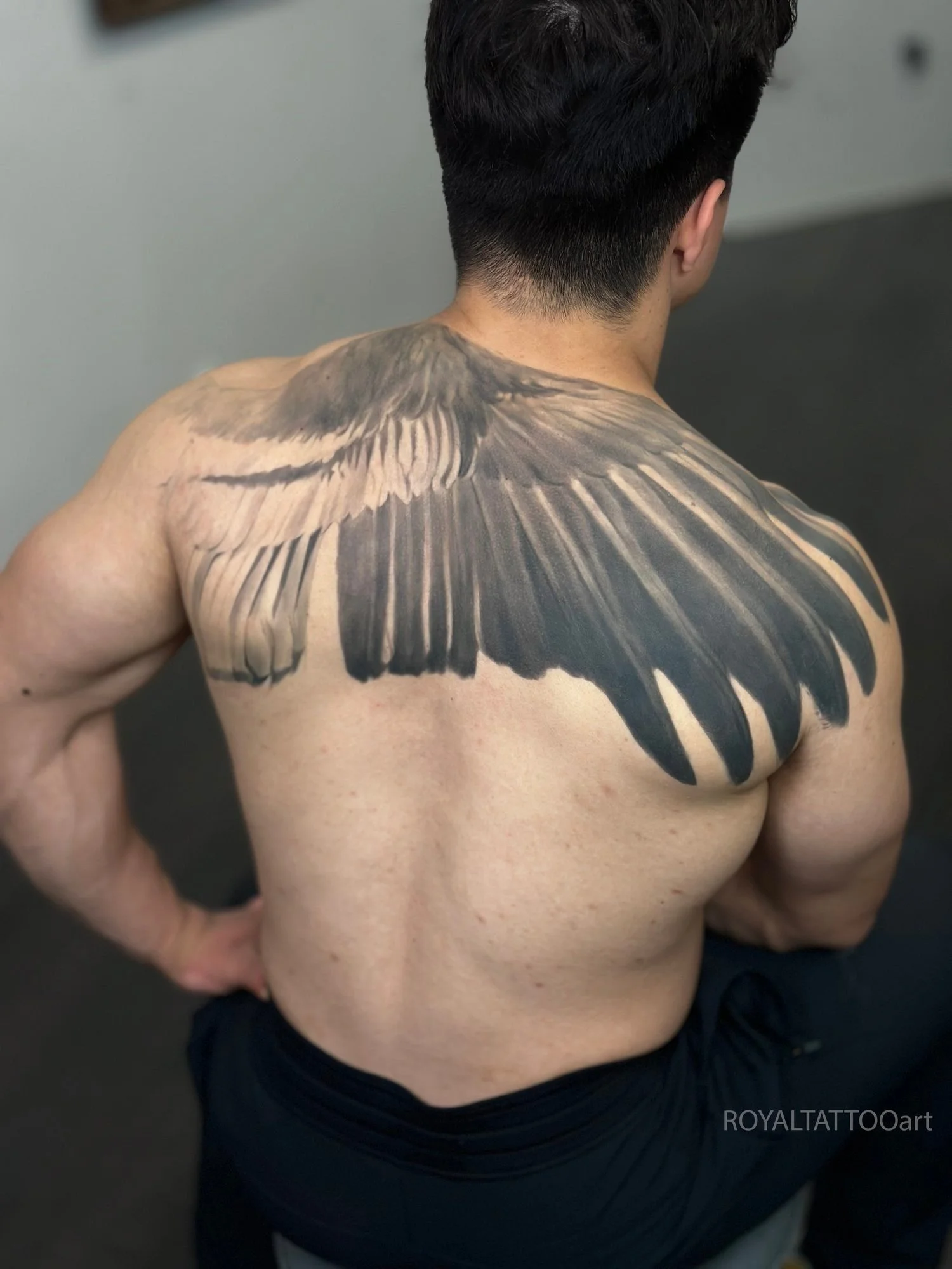 Black and grey realism back tattoo featuring a large eagle or condor wing, designed with realistic feather texture and strong movement.