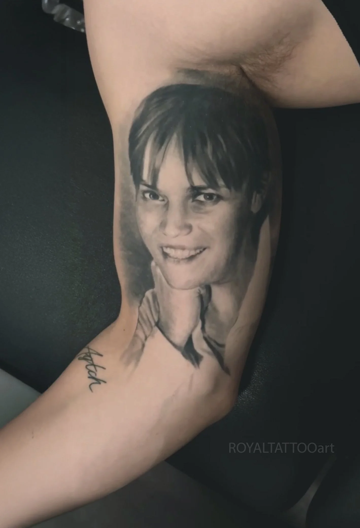 Black and grey smiling mother portrait tattoo on the inner arm, capturing a warm expression with smooth realistic detail by Royal Jafarov in NYC.