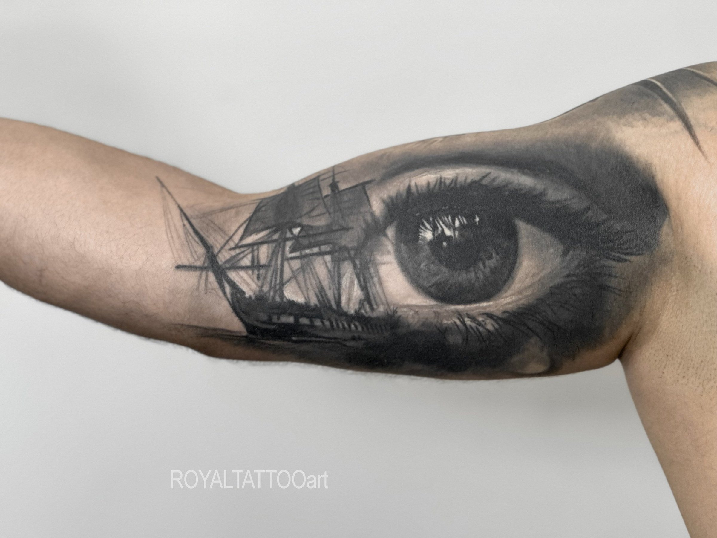 Black and grey realism tattoo featuring a detailed eye with ship imagery, combining portrait detail and nautical symbolism.