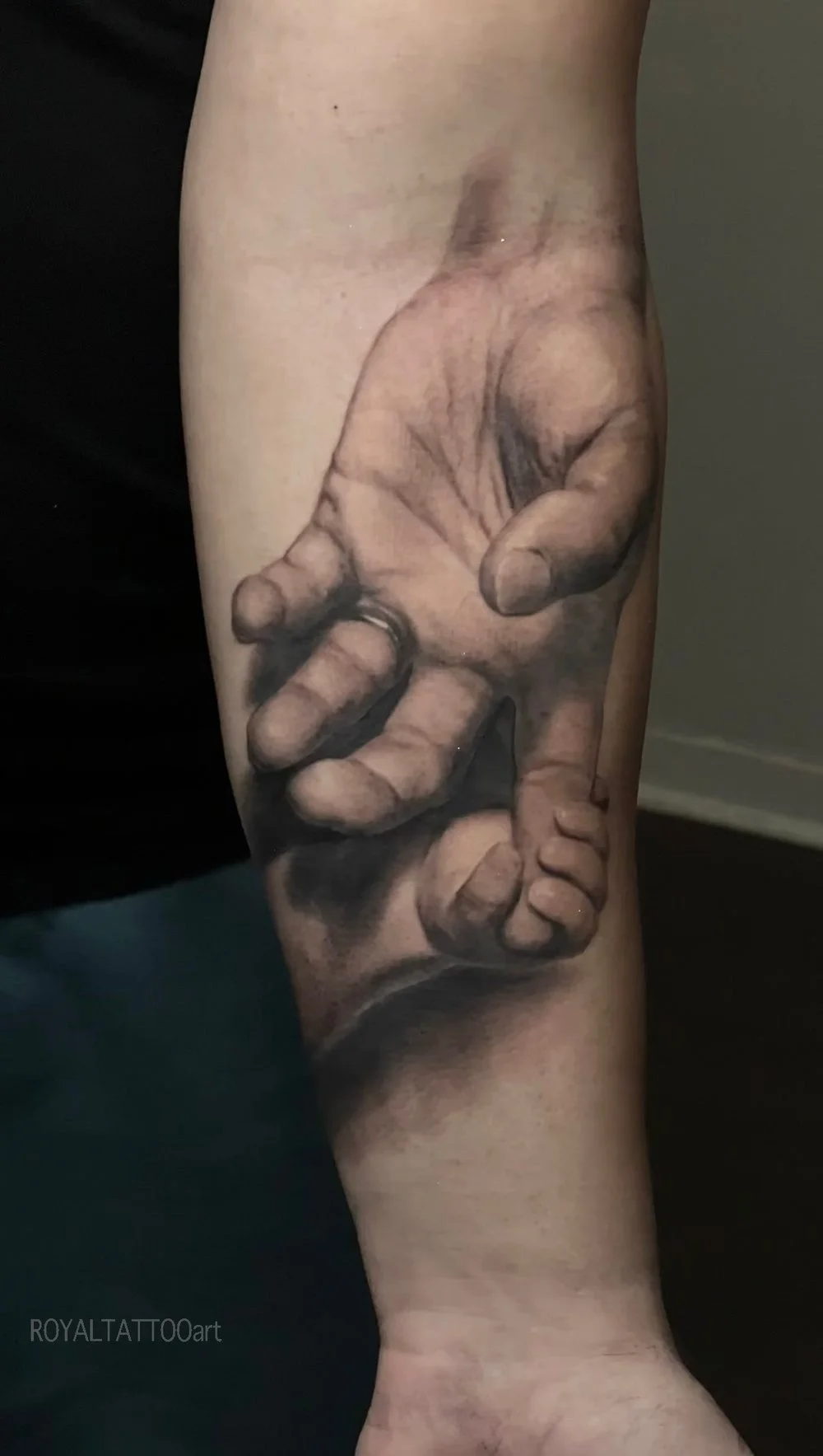 Black and grey realism forearm tattoo featuring a father and child hands design, created as a meaningful family tribute piece.
