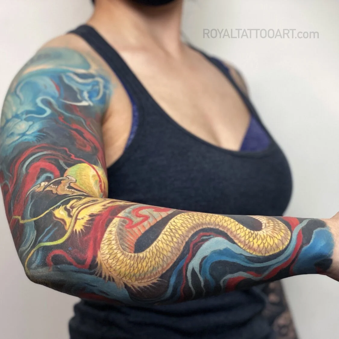 A dynamic Japanese dragon sleeve featuring swirling waves and a sinuous dragon rendered in vivid red and gold hues around the arm.