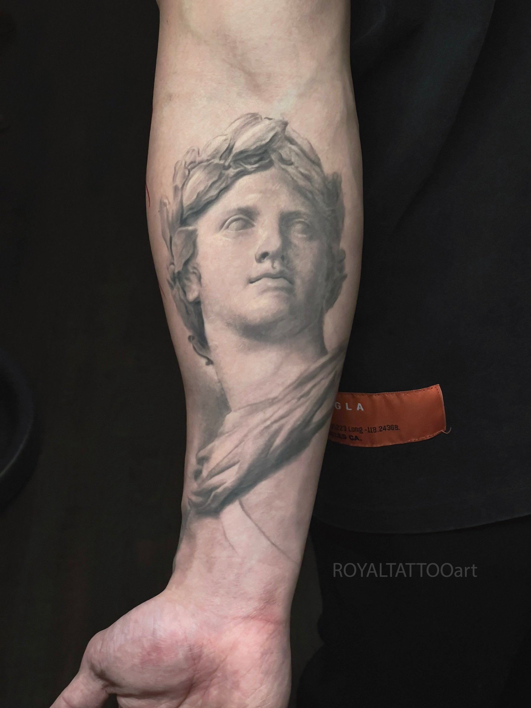 Black and grey portrait tattoo of a classical Greek statue on the forearm, rendered with stone-like texture and fine art realism by Royal Jafarov in NYC.