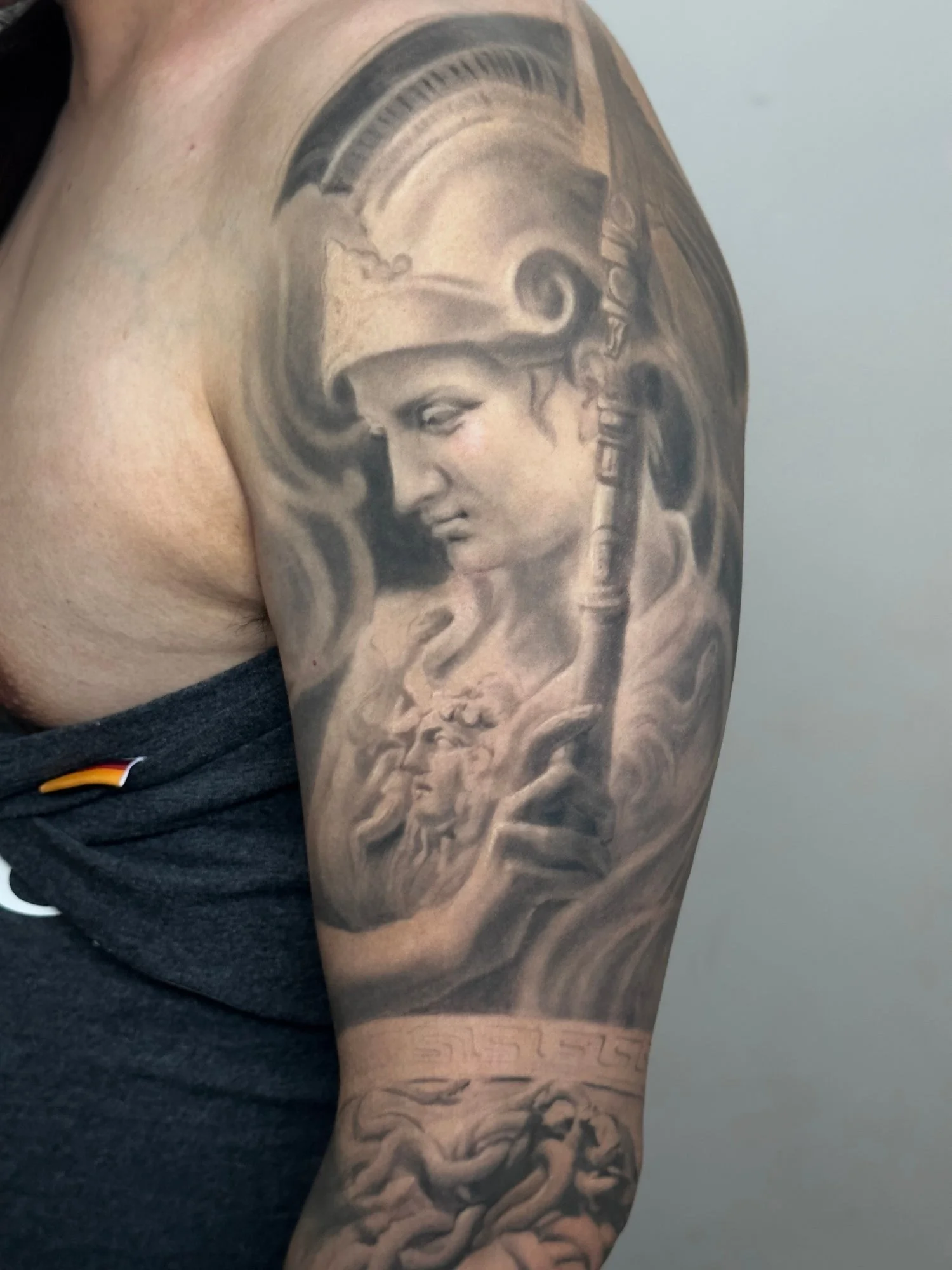 Black and grey mythology realism arm tattoo featuring Athena and Medusa-inspired imagery with classical detail and sculptural shading.
