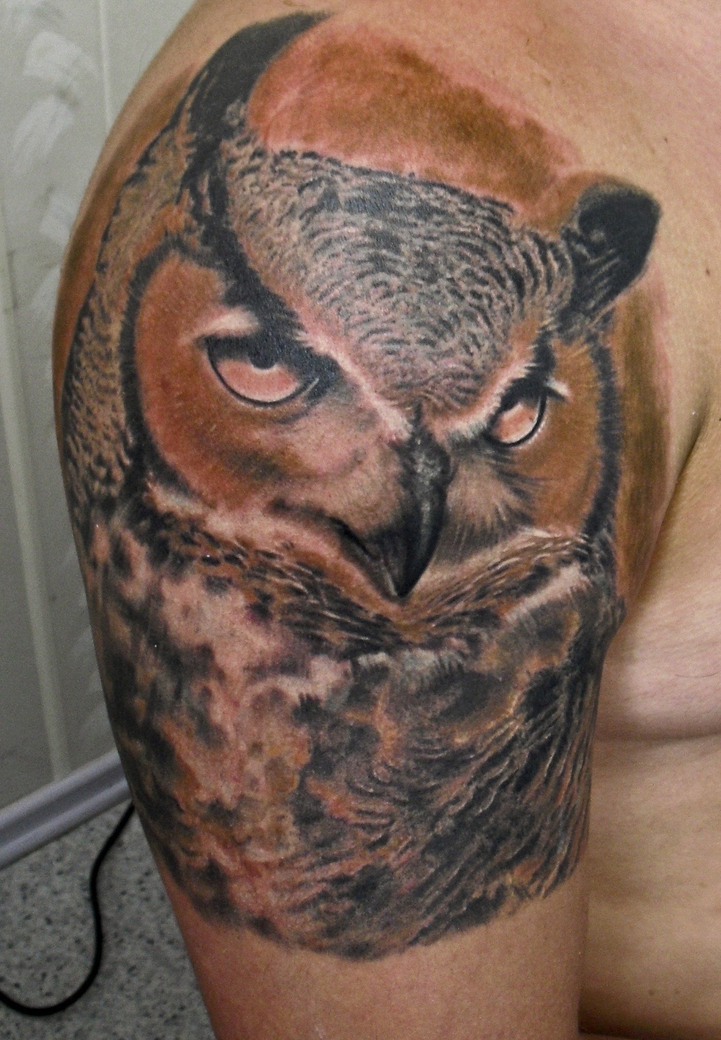 A realistic owl portrait tattoo on the thigh features intricate feather detail and piercing eyes, rendered in rich color realism.