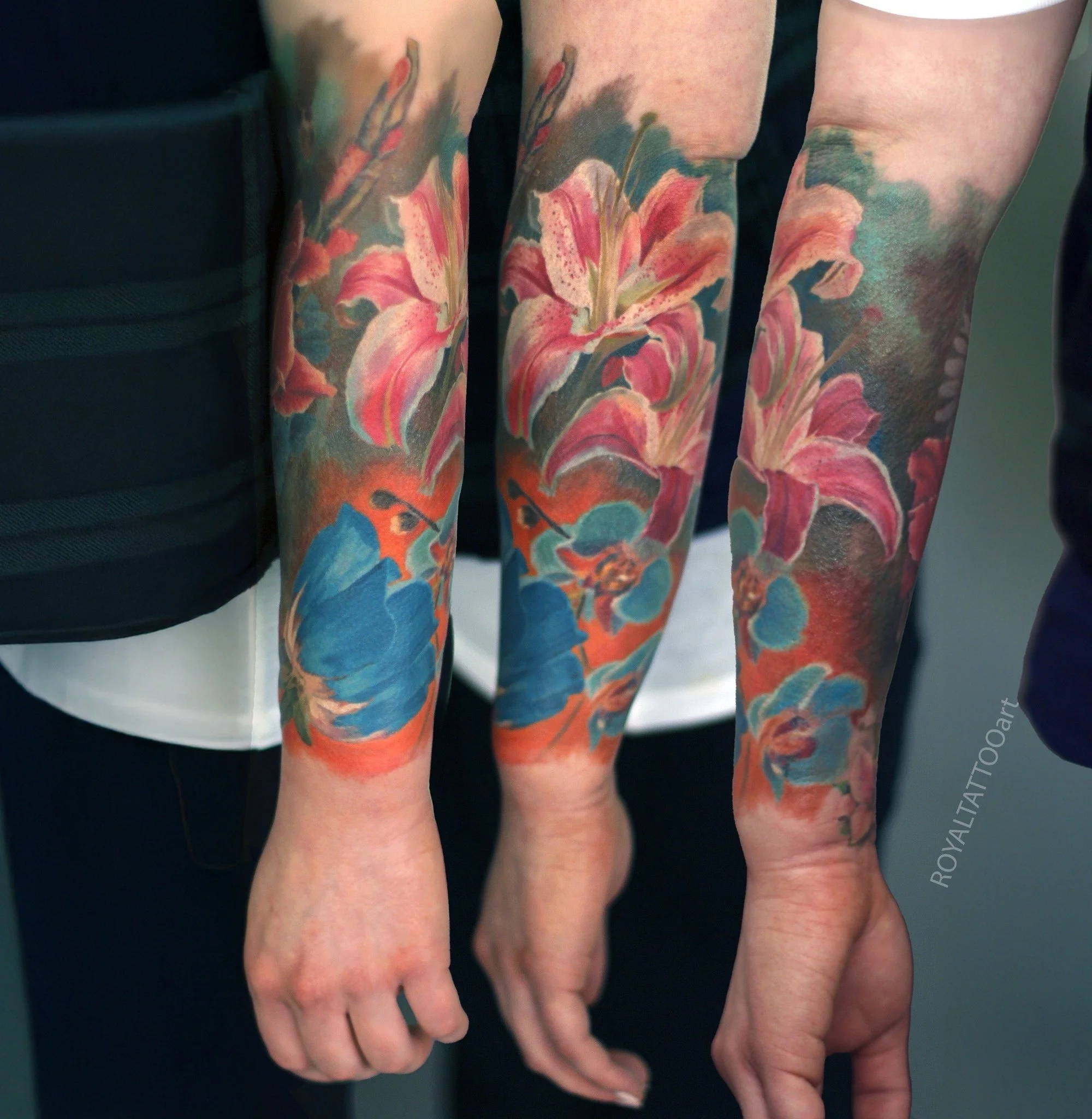 A vibrant forearm tattoo featuring pink lilies and lush foliage, rendered in stunning color realism.