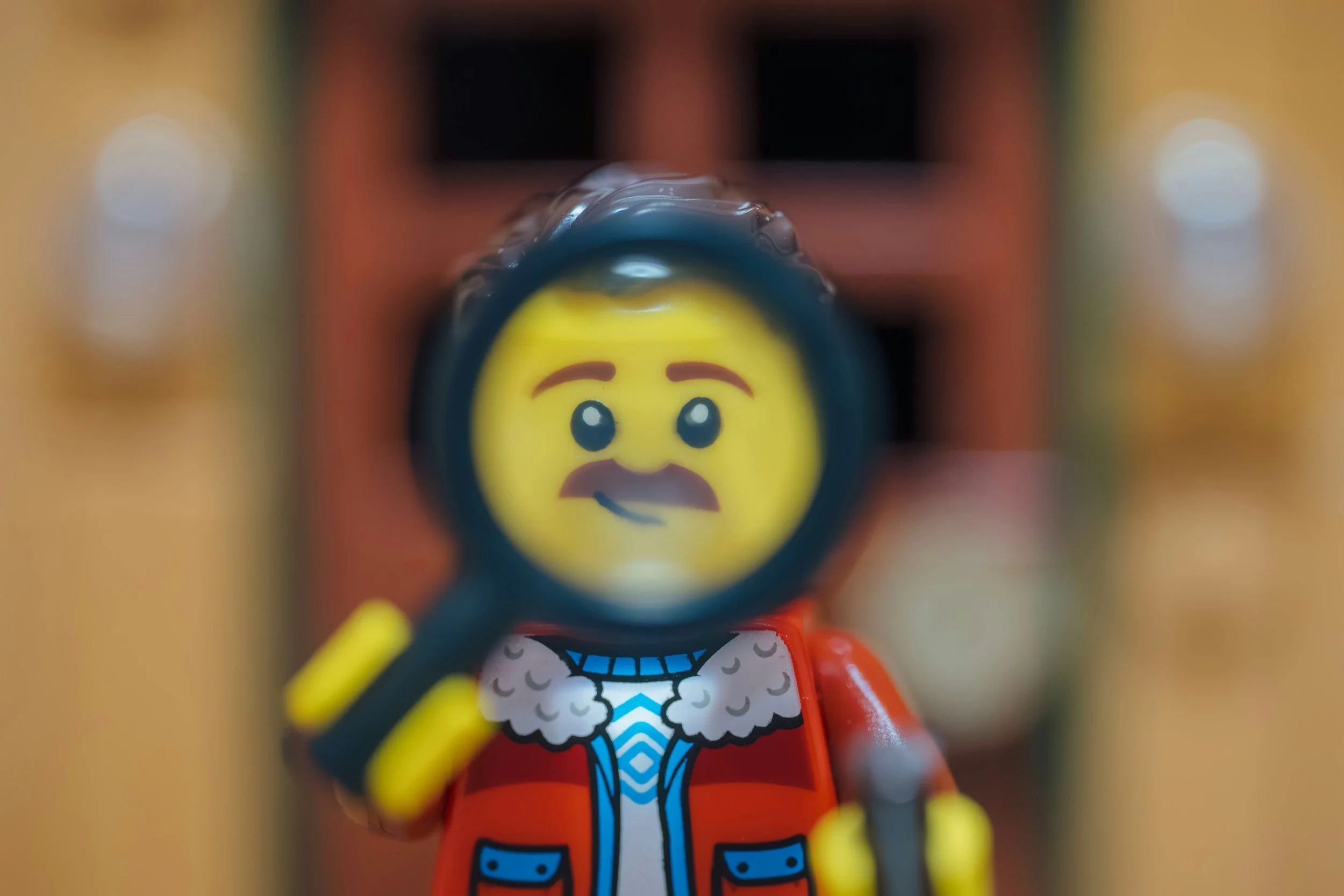 a LEGO minifigure with a brown mustache is holding a LEGO magnifying glass in front of his face