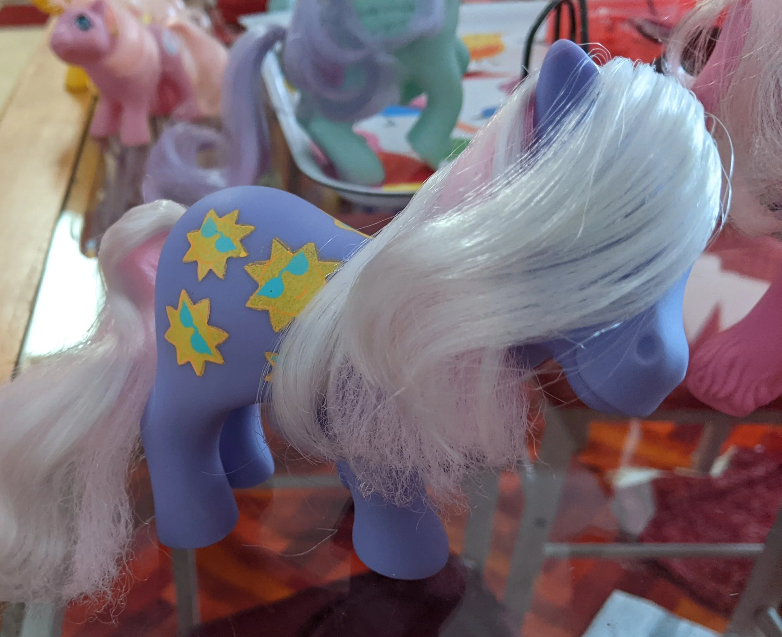A purple My Little Pony with bright yellow suns wearing sunglasses on her rear end, and really long white and pink hair, which is totally covering her face