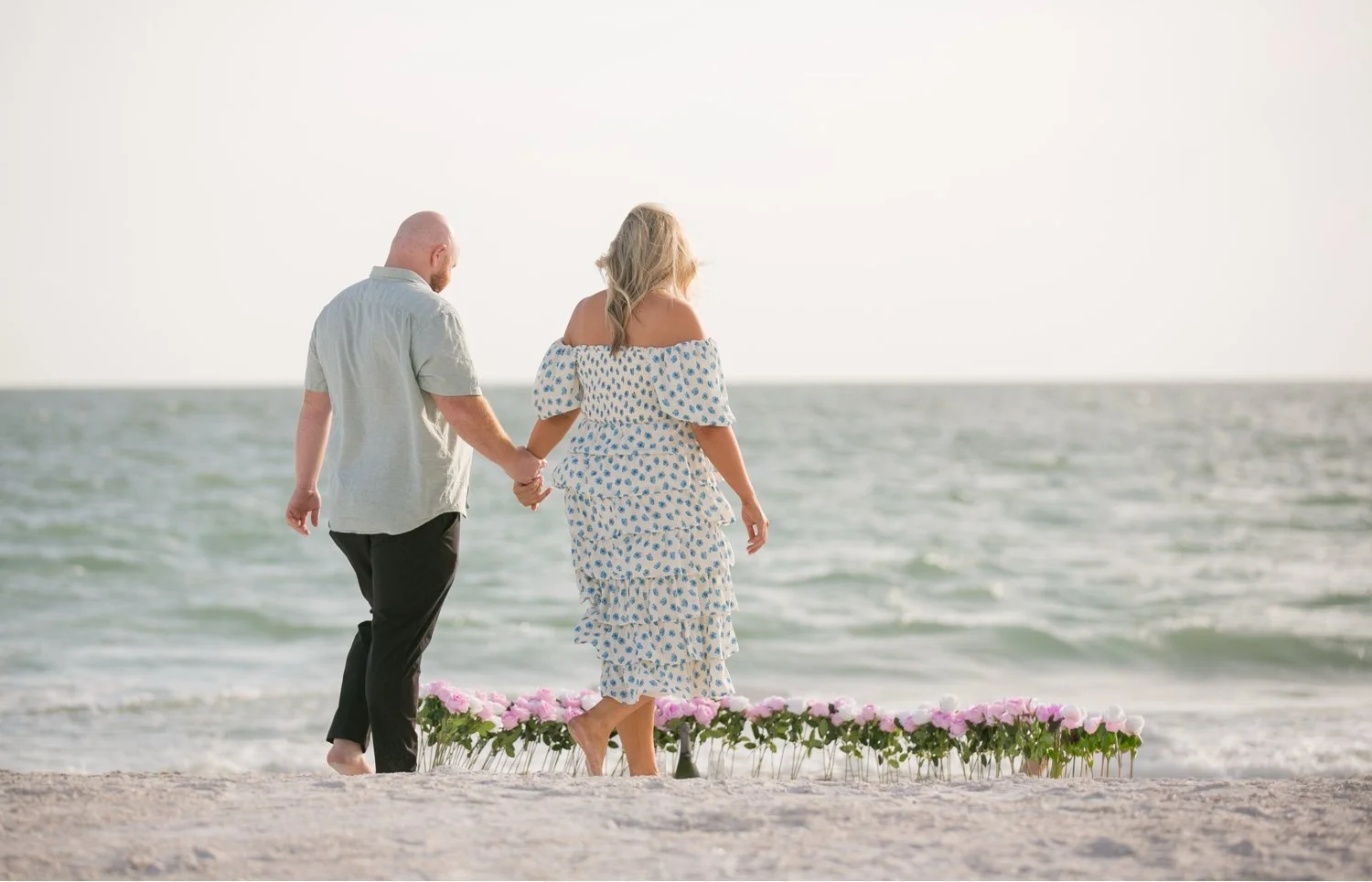 Couple walking toward a rose arch on the beach moments before a surprise proposal in St. Pete Beach
