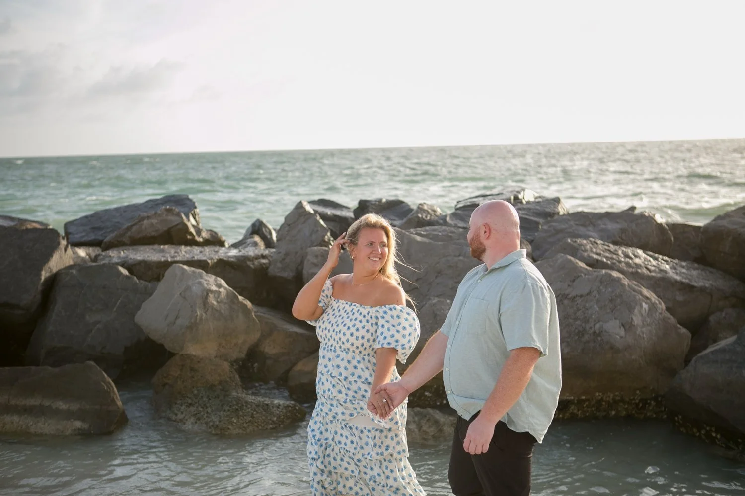 Newly engaged couple laughing by the Upham Beach breakwall in St. Pete Beach