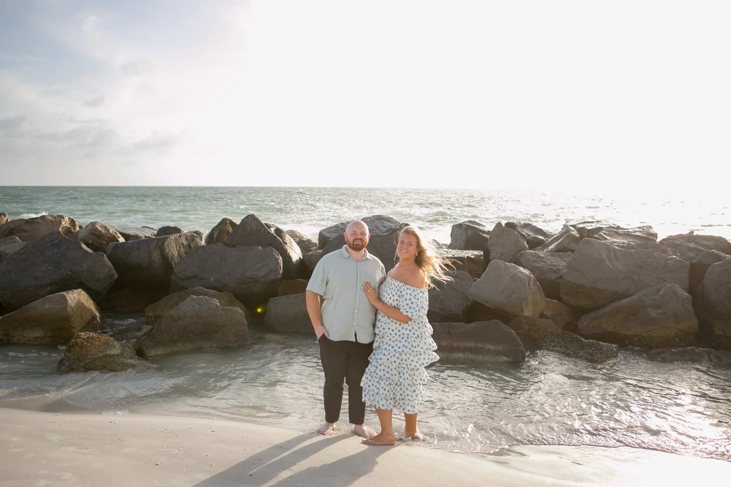 Engaged couple portrait in front of the Upham Beach rock breakwall at sunset
