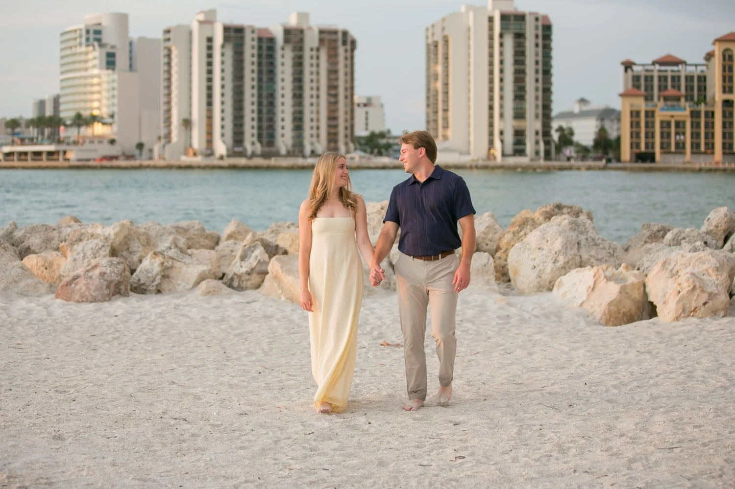 Engaged couple walking together near the jetty with Clearwater Beach hotels behind them