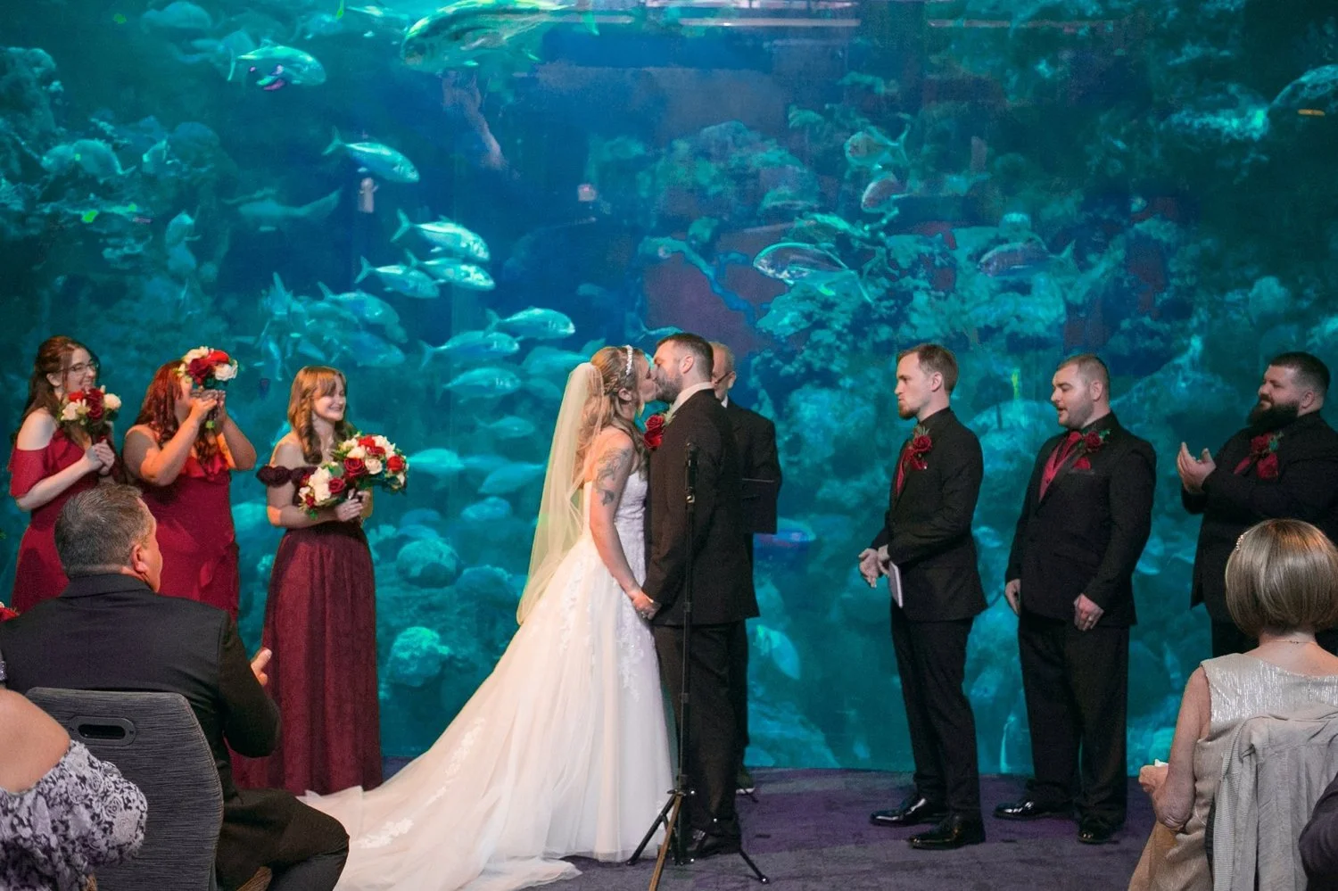 Bride and groom exchanging vows in front of the aquarium window with their wedding party