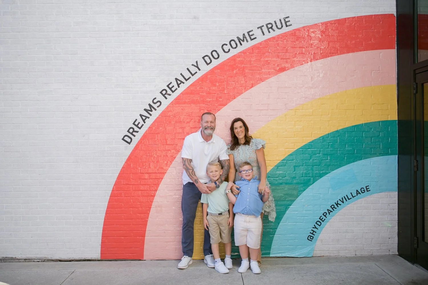 Family of four posing in front of the colorful rainbow mural at Hyde Park Village during Tampa family portraits