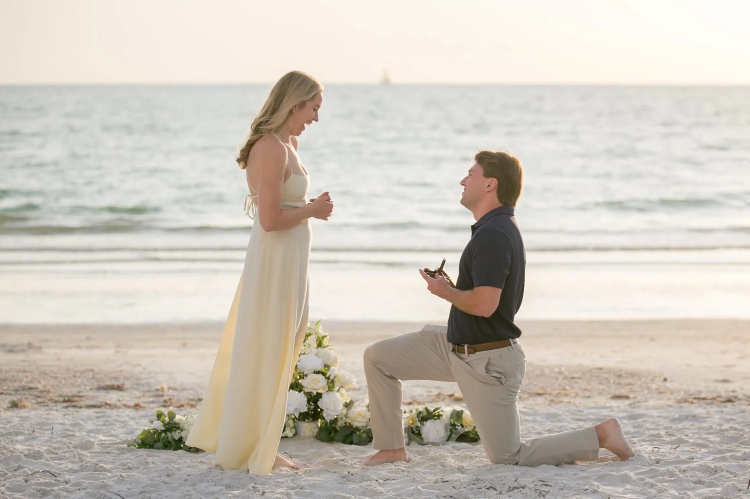 Groom-to-be on one knee proposing on Clearwater beach with floral arrangement