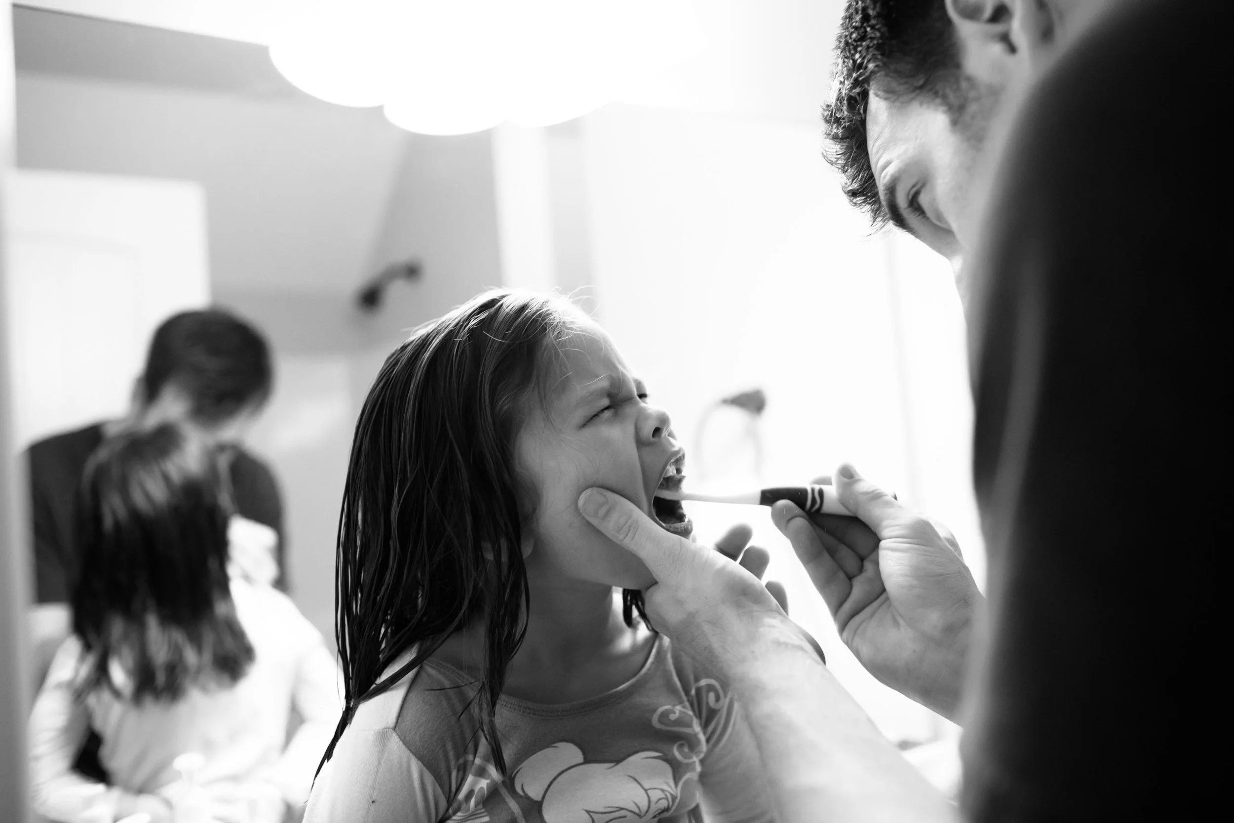 A girl with wet hair is getting her teeth checked by a dentist in a dental office. The dentist is examining her mouth with a mirror and is holding a dental instrument.