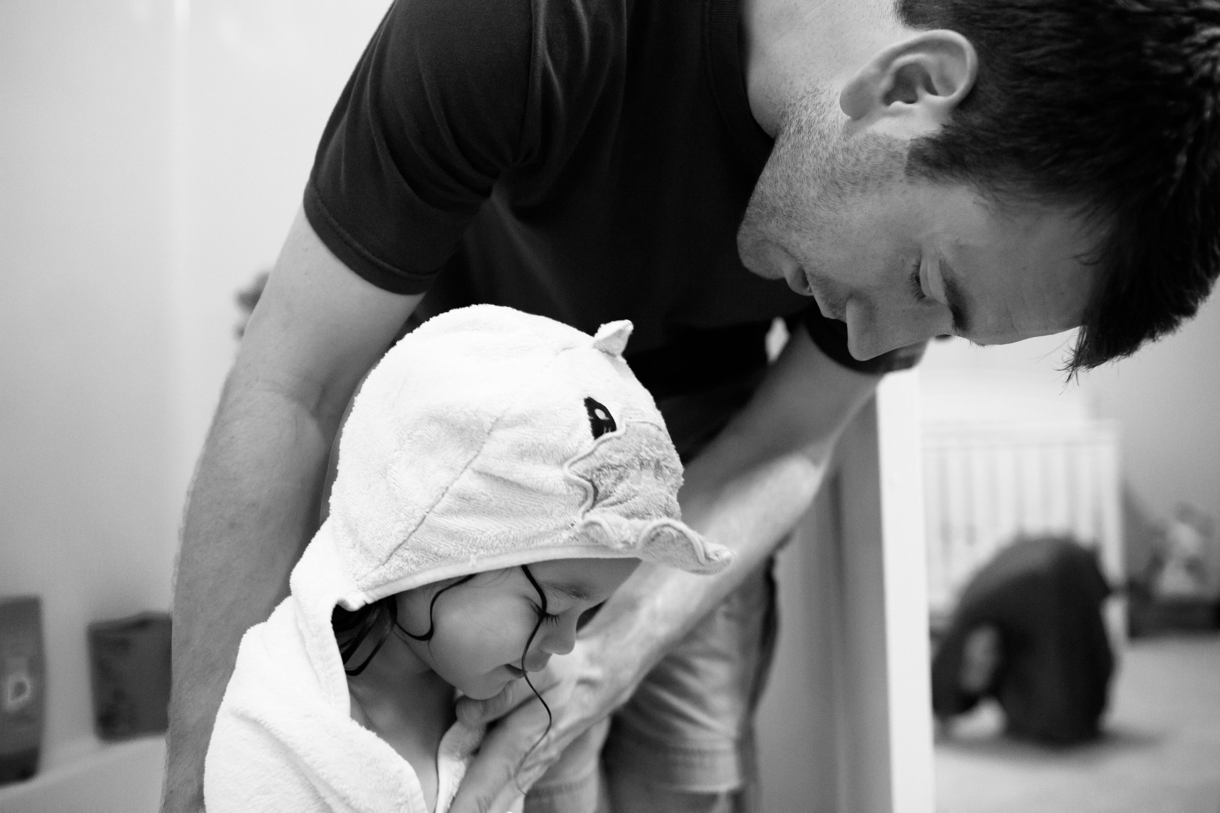 A man and a young girl, both with curly hair, looking downward, possibly at something they are holding or doing together, in an indoor setting.