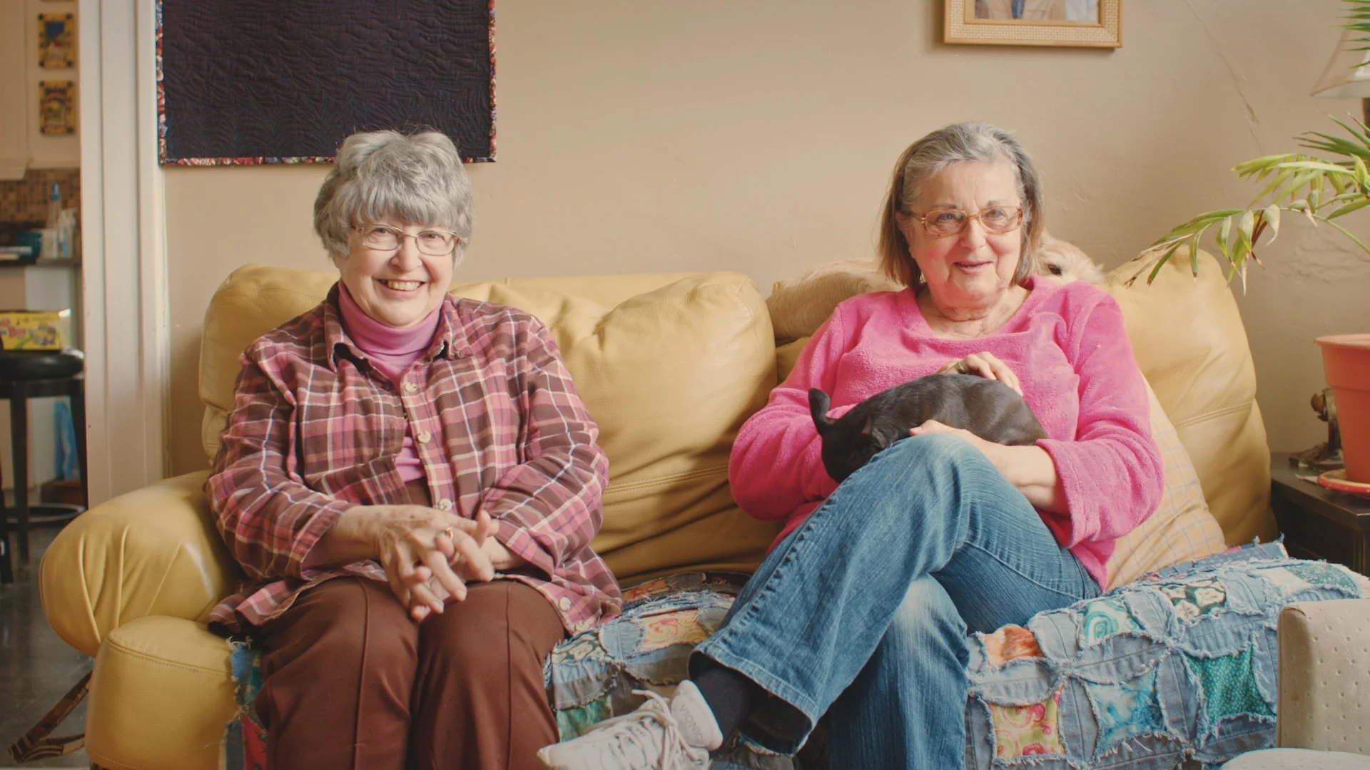 Still from SXSW Short Film Quilt Fever  Directed by Olivia Loomis Merrion featuring 2 women  sitting on a quilt holding what looks like a small dog.