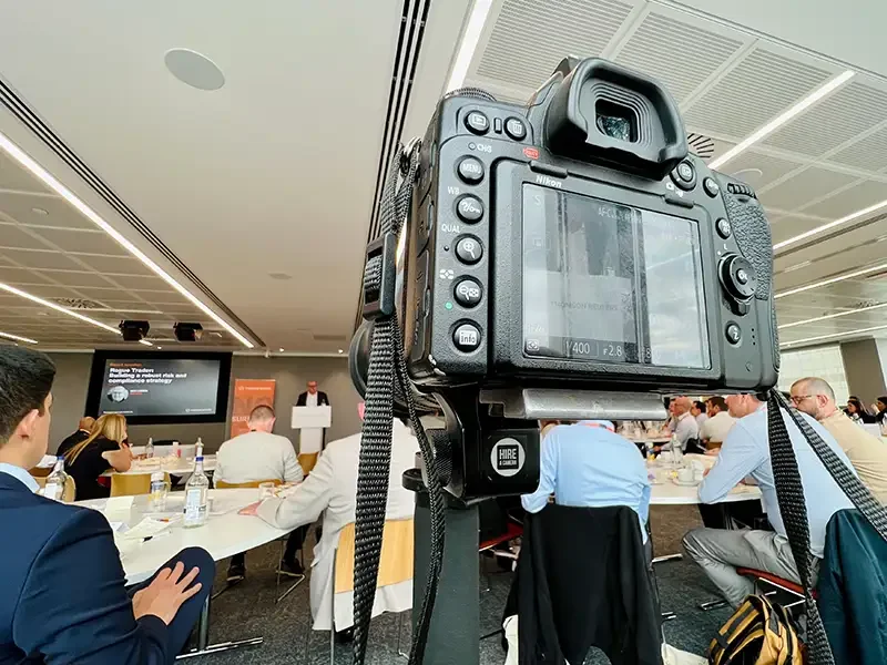 A professional editorial camera with a long telephoto lens focused on a major conference stage, demonstrating the high-pressure PR and press coverage provided by Scott Ramsey Photography & Videography.