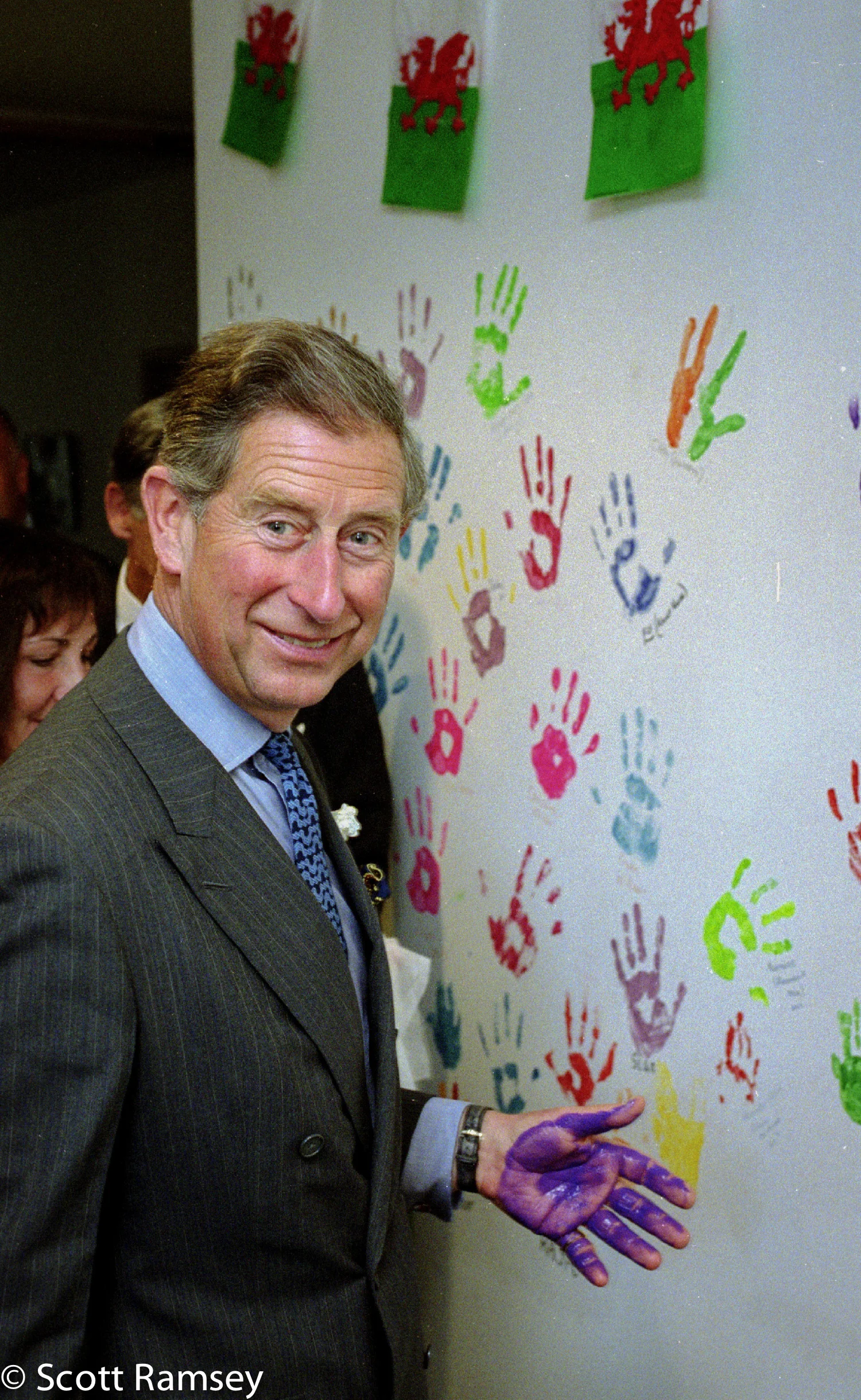 King Charles III (then HRH The Prince of Wales) laughing with a purple handprint at Ty Hafan Children’s Hospice. An iconic frame from Scott Ramsey’s editorial photography archive, documenting British history since 1988.