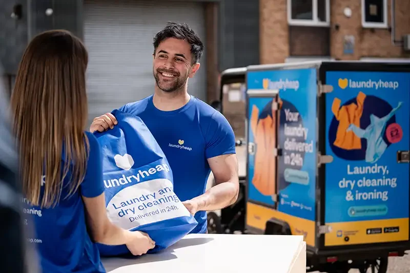 A professional editorial PR photograph for Laundryheap, showing branded staff in a real-world delivery scenario, captured by Scott Ramsey to demonstrate high-end commercial storytelling.
