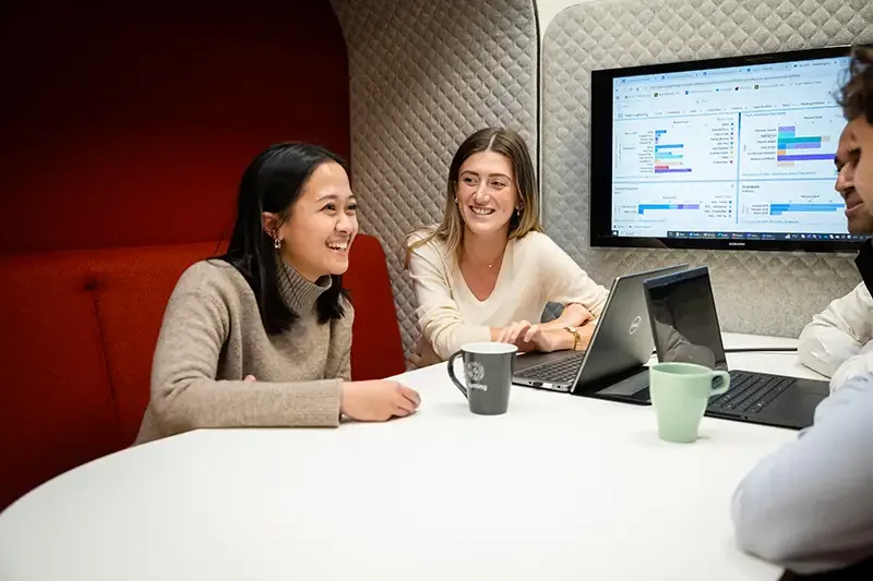A professional corporate photography shot of a female leader and her team engaged in an informal business meeting, capturing authentic company culture and high-end executive portraiture in a modern London office.