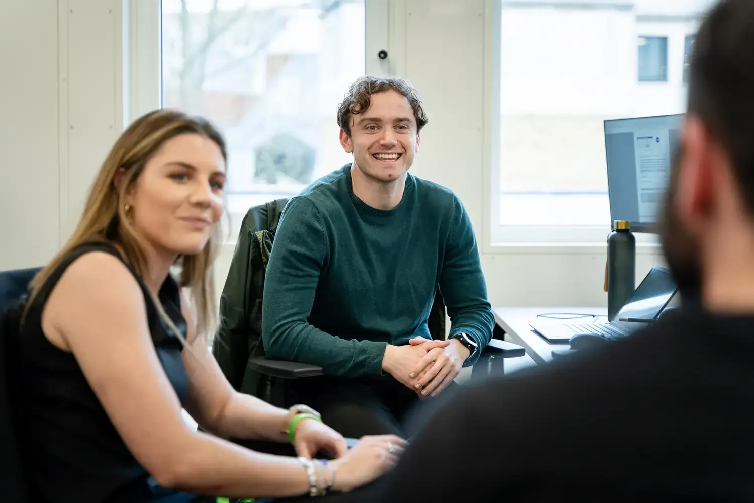 Candid corporate photography of a relaxed team meeting in a modern London office. Young professionals chatting and smiling, illustrating positive company culture. Shot by Scott Ramsey.