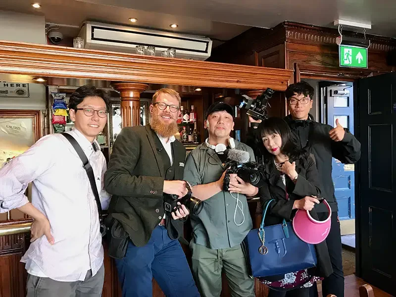 Scott Ramsey on location with the South Korean MBC production crew at an English pub in London. This image documents the professional team behind the 'Forbidden Alleys' documentary series.