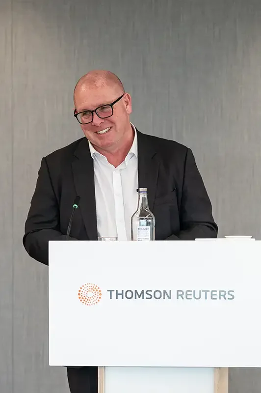 Nick Leeson delivering a keynote speech at a branded Thomson Reuters podium in London. Professional PR and event photography by Scott Ramsey Photography & Videography, highlighting brand impact and high-profile speaker coverage.
