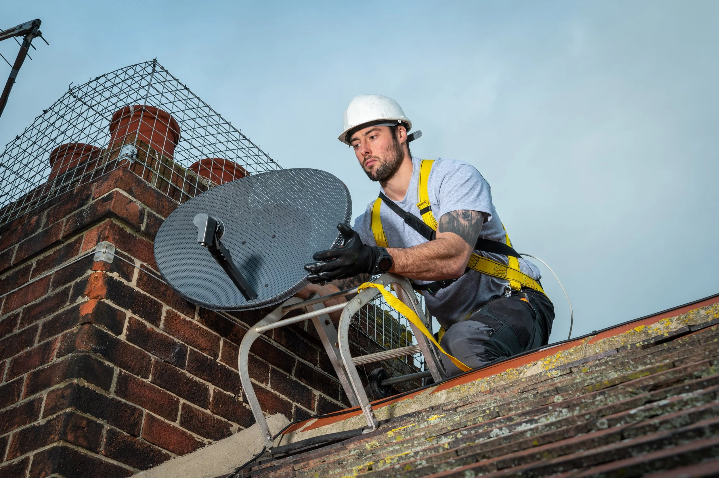 A professional commercial photograph of a technical engineer installing satellite equipment on a roof, demonstrating Scott Ramsey's ability to capture high-end industrial and technical assets on location.
