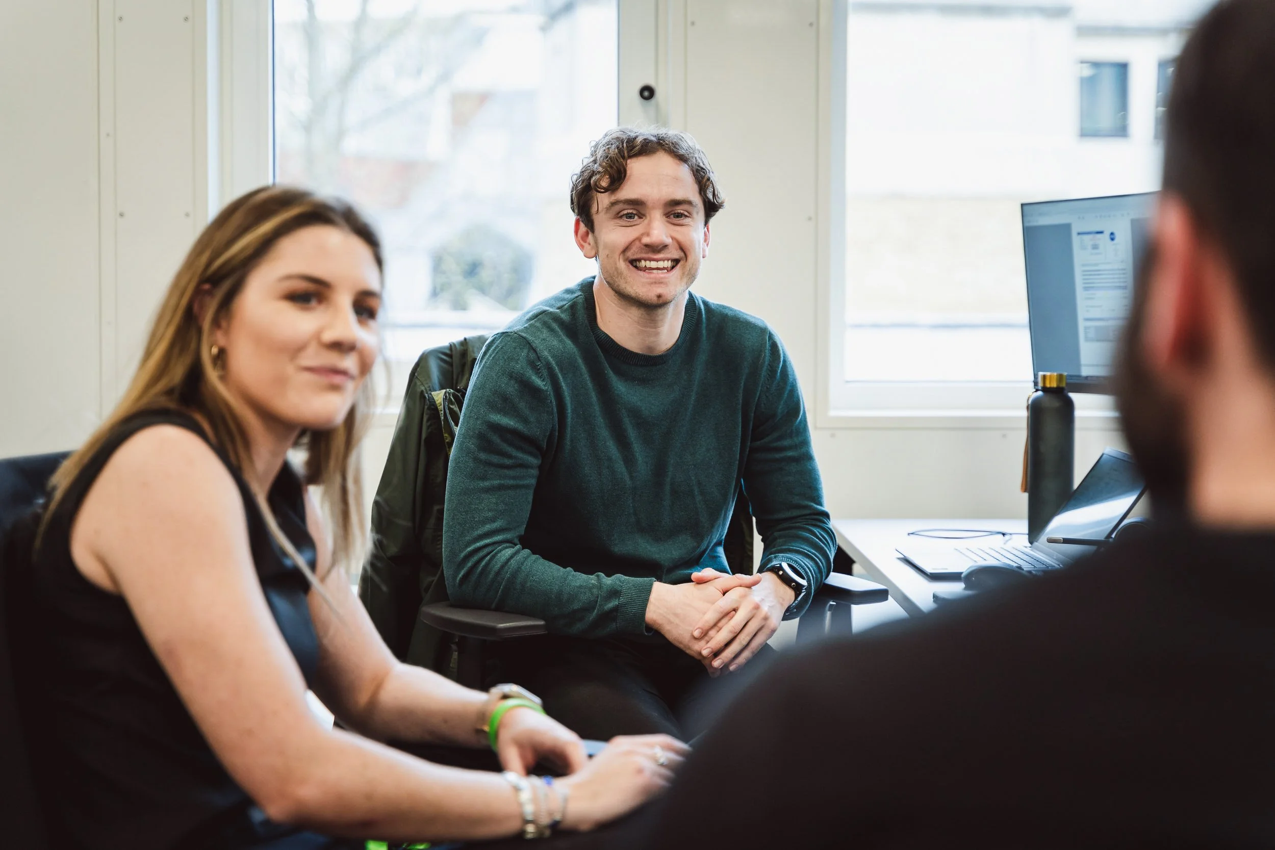 A cinematic shot of a male and female executive in smart-casual attire sharing a relaxed conversation in a modern office, showcasing an authentic and collaborative corporate culture.