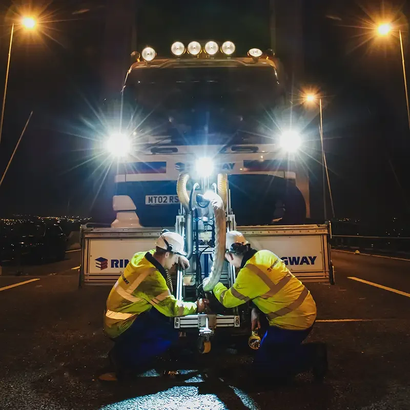 Commercial photography by Scott Ramsey: Ringway workers operating a road resurfacing machine at night on the M25 QE2 Bridge.