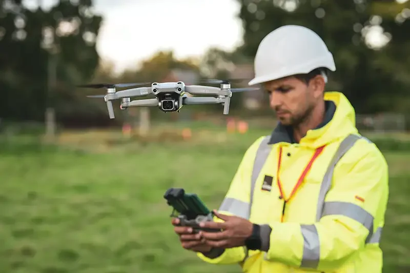 Professional drone pilot in full PPE operating a commercial flight for an industrial client in the UK.