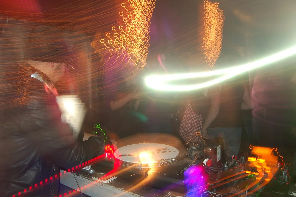 A DJ performing at a nightclub with colorful light streaks and a blurred crowd in the background.