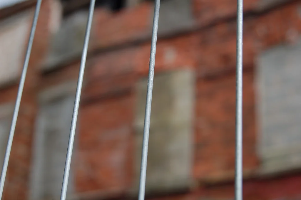 Close-up of metal wire fence with a brick building in the background.