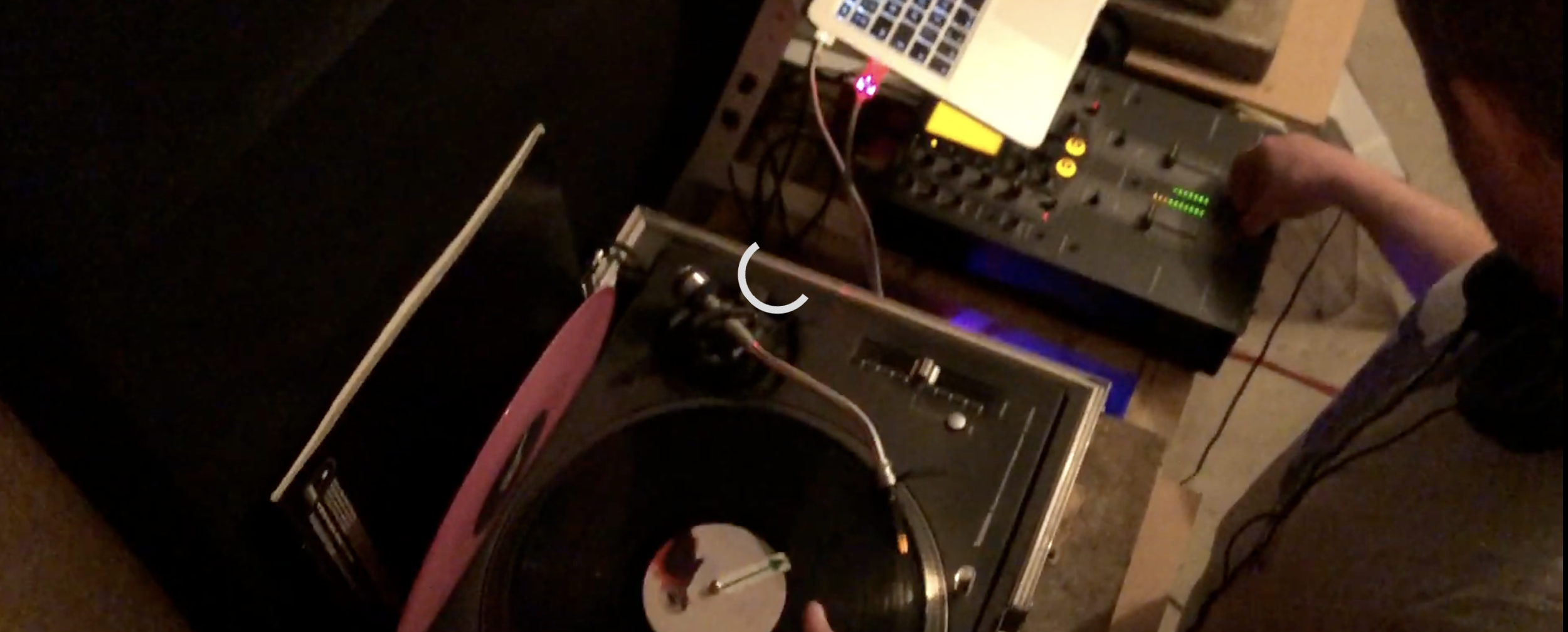DJ mixing music with turntables and a laptop in a dimly lit room.
