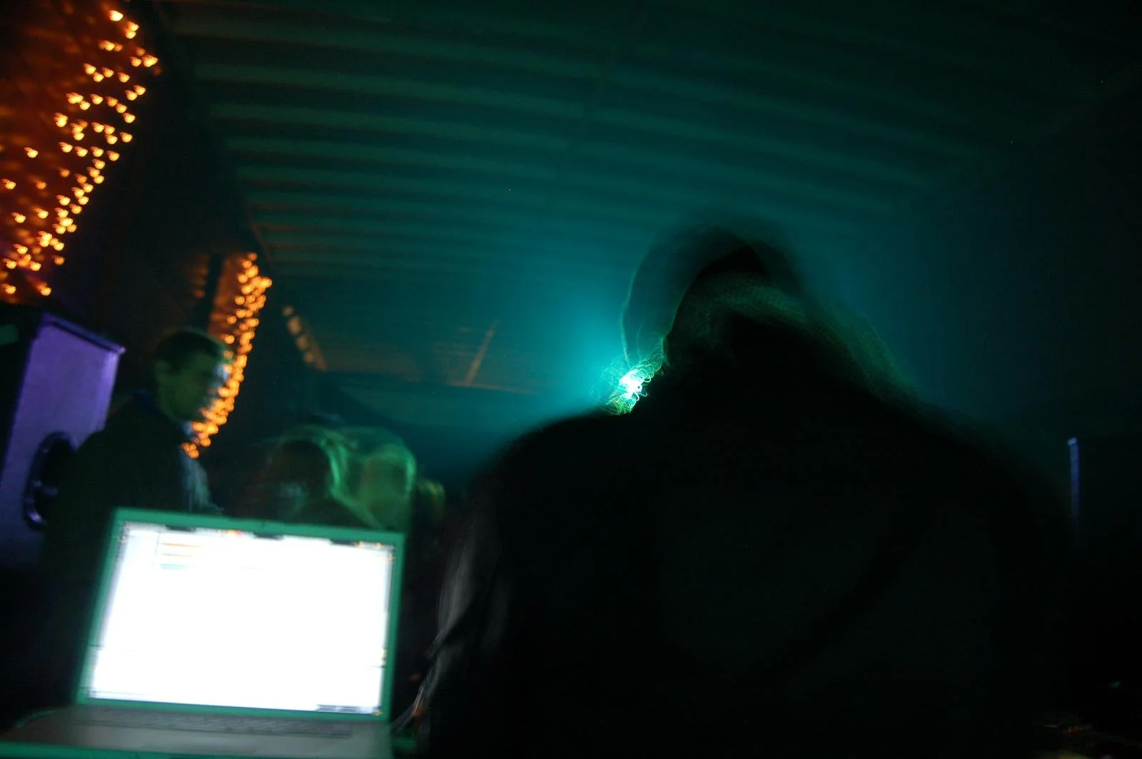 People in a dark room with colorful lights and a laptop with a bright screen