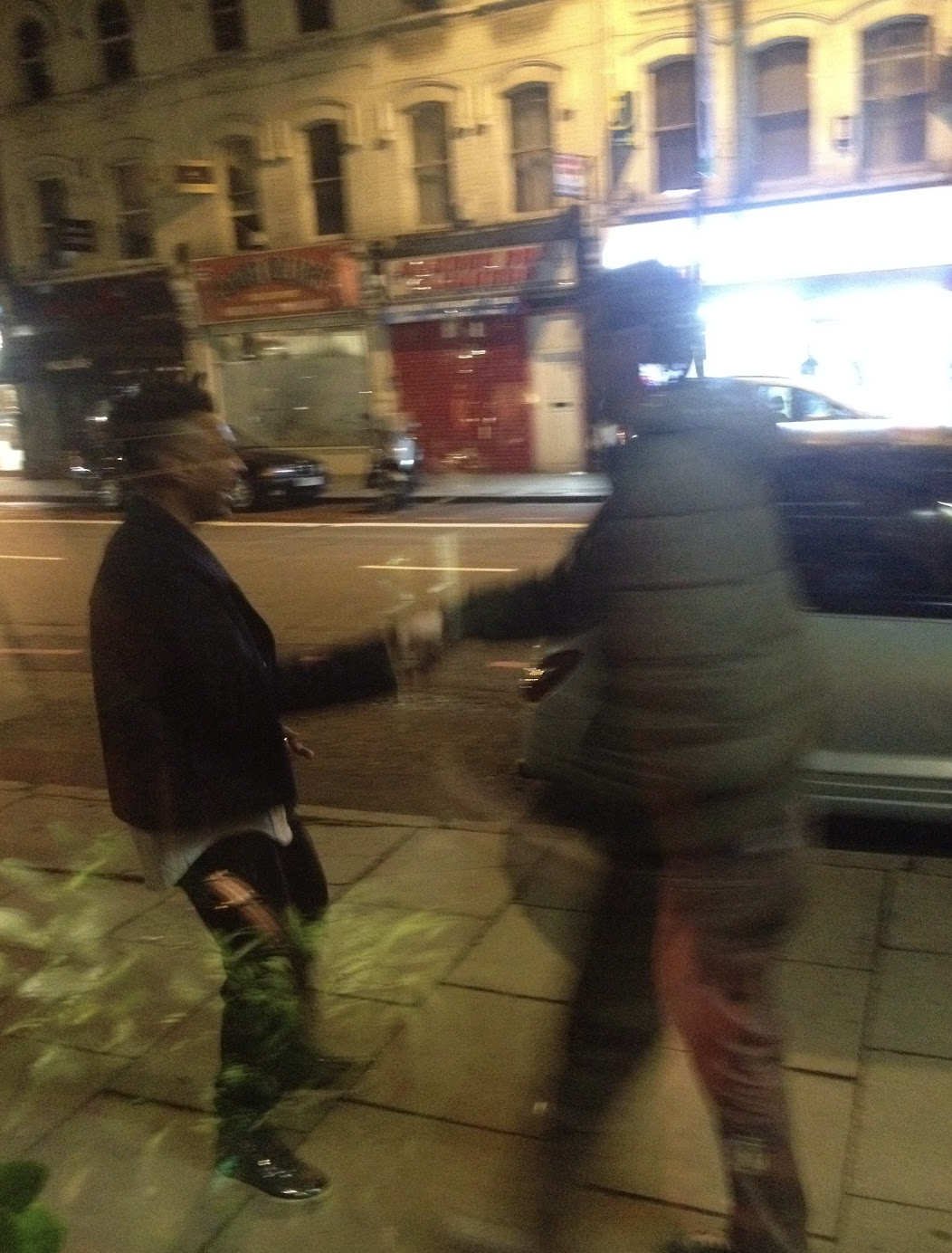 Two men exchanging fists in a street at night, with buildings and parked cars in the background.