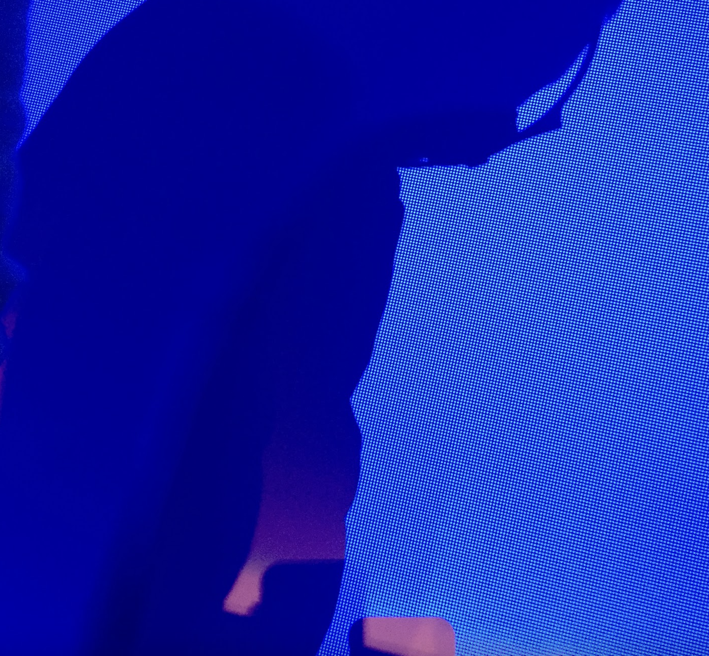 Person taking a selfie in front of a bright digital screen, creating a silhouette in the dark.