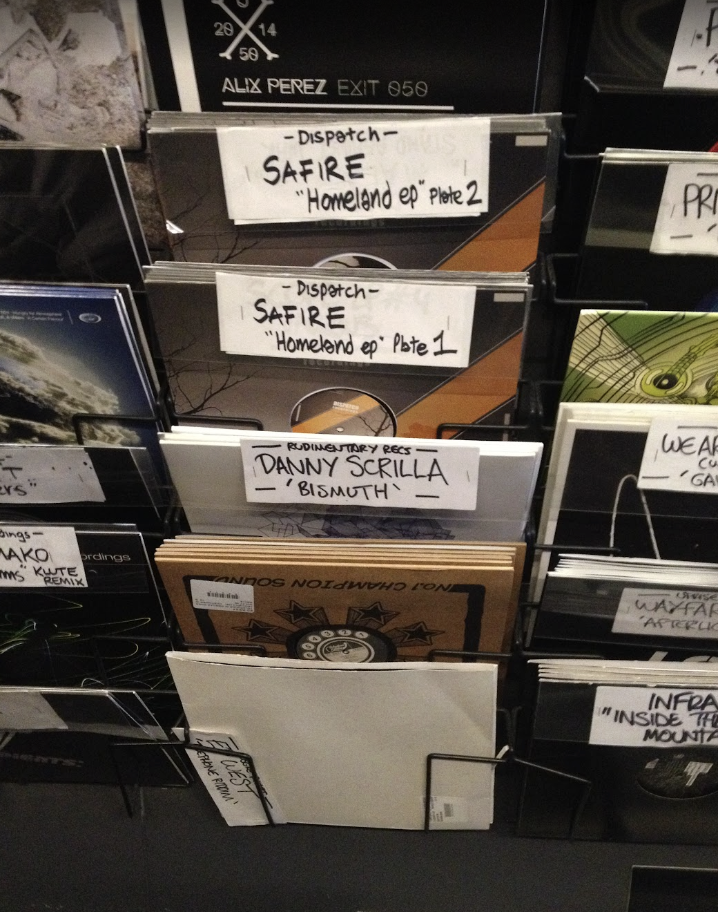 A display of vinyl records with handwritten labels, featuring albums including 'Homeland' Part 1 and 2 by Safire, and a record by Danny Scrilla titled 'Bismuth'.
