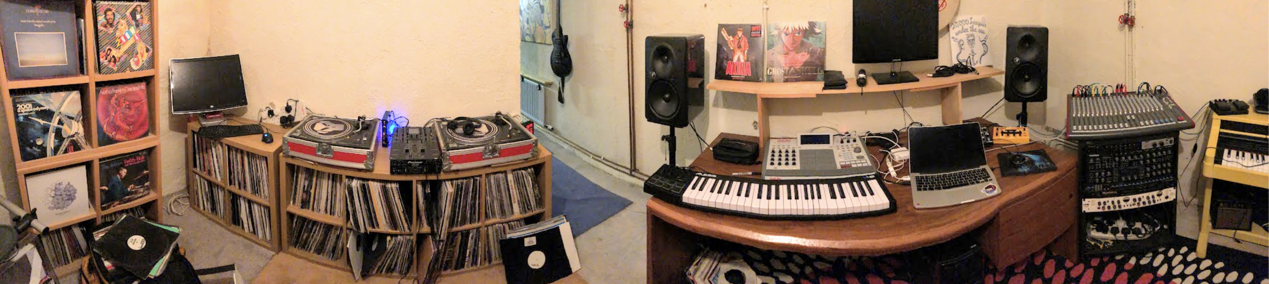 A music studio with vinyl records, DJ turntables, a keyboard, a laptop, and stereo speakers, decorated with posters on the walls.