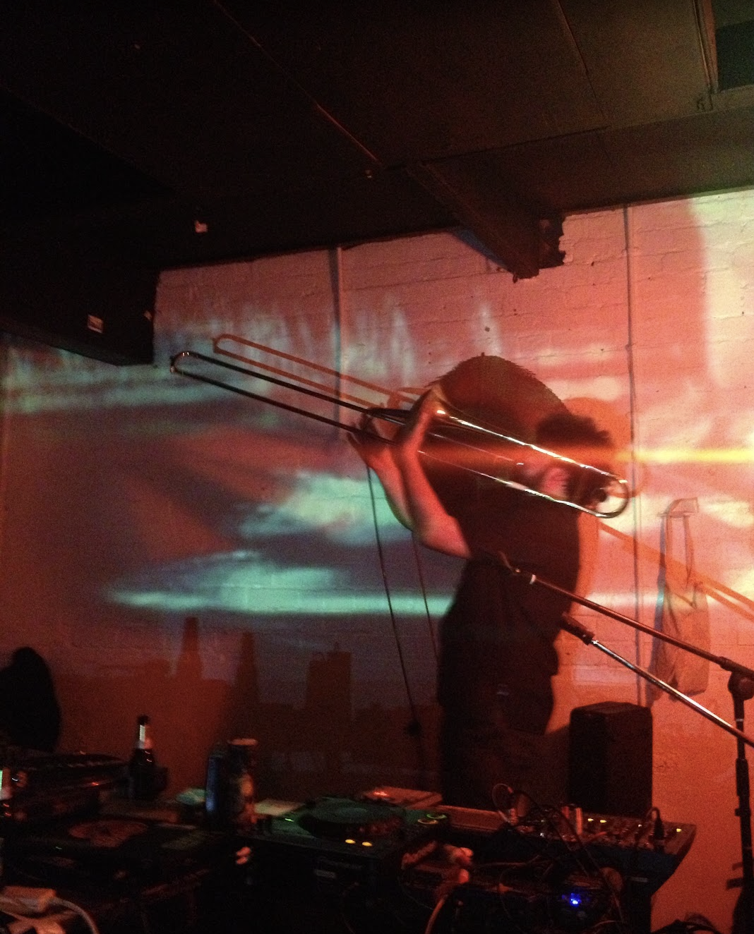 A person holding a trombone with colorful lights and projections on a brick wall behind them.