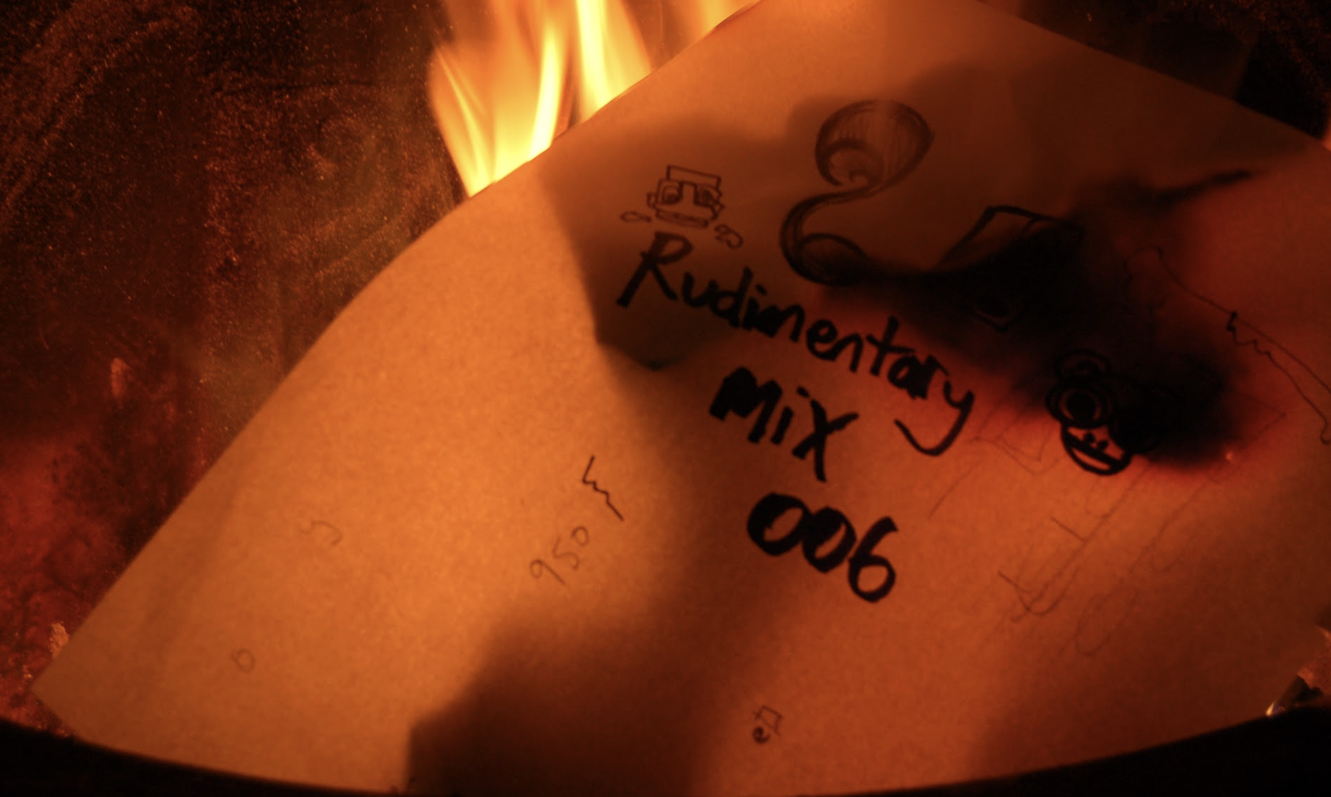 A burning paper with handwritten notes, showing the words 'Rudimentary Mix 906' and some drawings, with flames in the background.